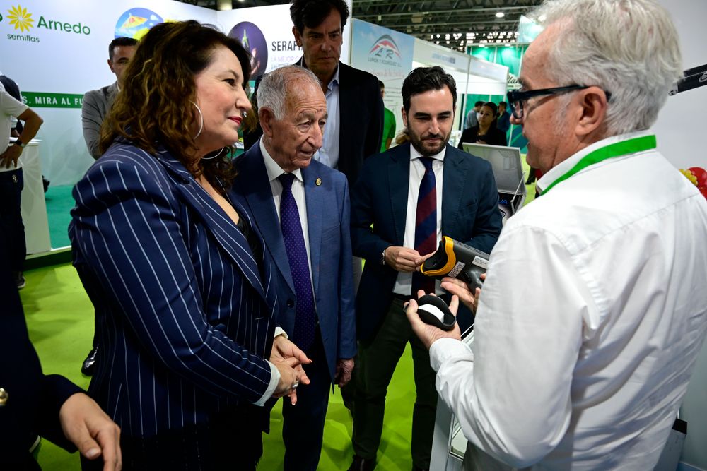 Un expositor muestra uno de sus productos a las autoridades que se acercan a su stand durante su recorrido por Infoagro Exhibition 2025